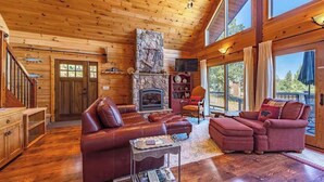 A log cabin interior with a stone fireplace, leather sofas, and large windows. - Straight From The Heart (Lyle)