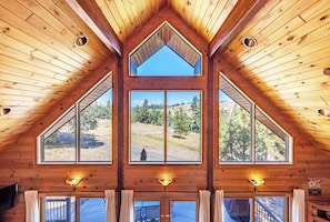 A wooden interior with a high ceiling, large windows, and a view of a forested landscape. - Straight From The Heart (Lyle)