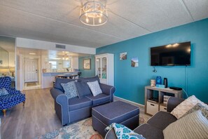 Ein Wohnzimmer mit blauer Wand, einer Sofagarnitur, einem Fernseher und einem Couchtisch.