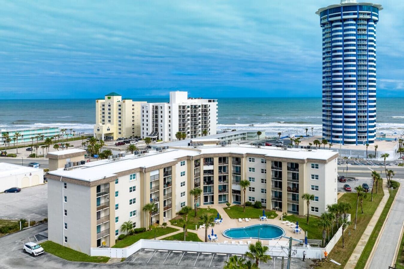 Ein Hotel mit Pool, Blick auf den Strand und einem hoch aufragenden Gebäude in der Nähe.