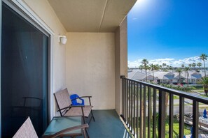 Ein Balkon mit zwei Stühlen, einem kleinen Tisch und Blick auf eine Wohngegend mit Palmen und Häusern.