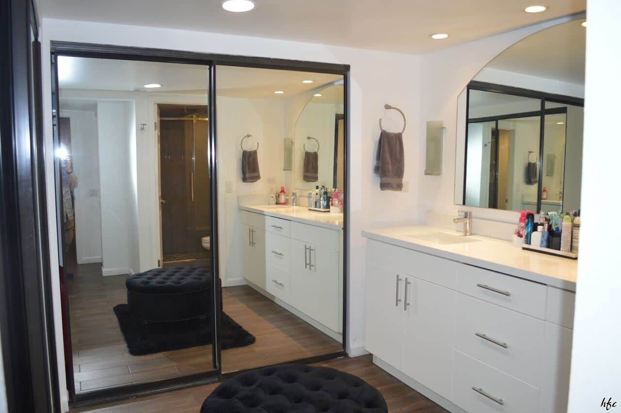 A modern bathroom with a glass shower enclosure, white cabinetry, and a large mirror.
