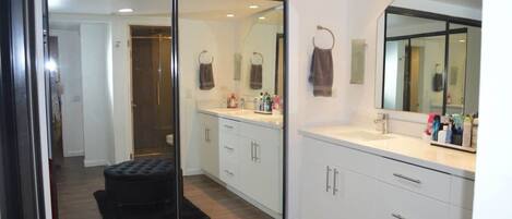 A modern bathroom with a glass shower enclosure, white cabinetry, and a large mirror.
