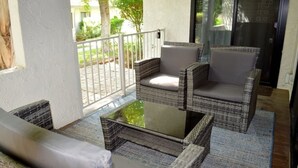 Un balcón con muebles de mimbre y una mesa de vidrio, con vistas a un jardín.