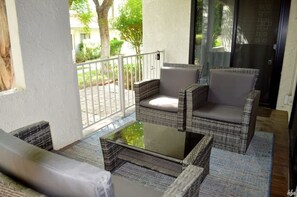 Ein Balkon mit Korbmöbeln und einem Glastisch, mit Blick auf einen Garten.