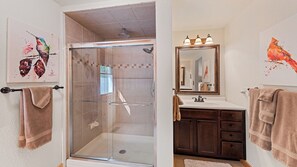 A bathroom with a glass shower enclosure, a sink with a mirror, and artwork on the walls. - Beautiful and comfy mountain view home with outdoor living showcased! (Waynesville)