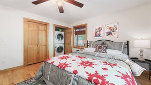 Ein Schlafzimmer mit Bett, Nachttisch, Lampe, Deckenventilator, Waschmaschine und Holztüren.