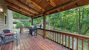Eine Holzterrasse mit Grill, Stühlen und Blick auf einen Wald.