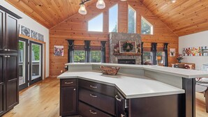 Et rummeligt køkken med en stenspejs, træloft og store vinduer.