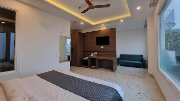 Ein modernes Schlafzimmer mit Bett, Deckenventilator, Einbauleuchten, Fernseher, einer Sitzecke mit Sofa und einem großen Fenster.