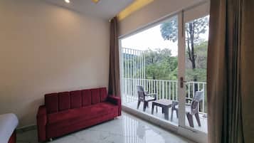 Una habitación con un sofá rojo, una cama, un balcón con mesa y sillas, y vistas a árboles.