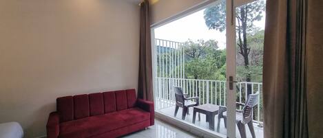 Una habitación con un sofá rojo, una cama, un balcón con mesa y sillas, y vistas a árboles.
