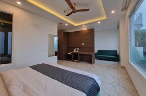 A modern bedroom with a large bed, a ceiling fan, a seating area with a sofa, and a large window.