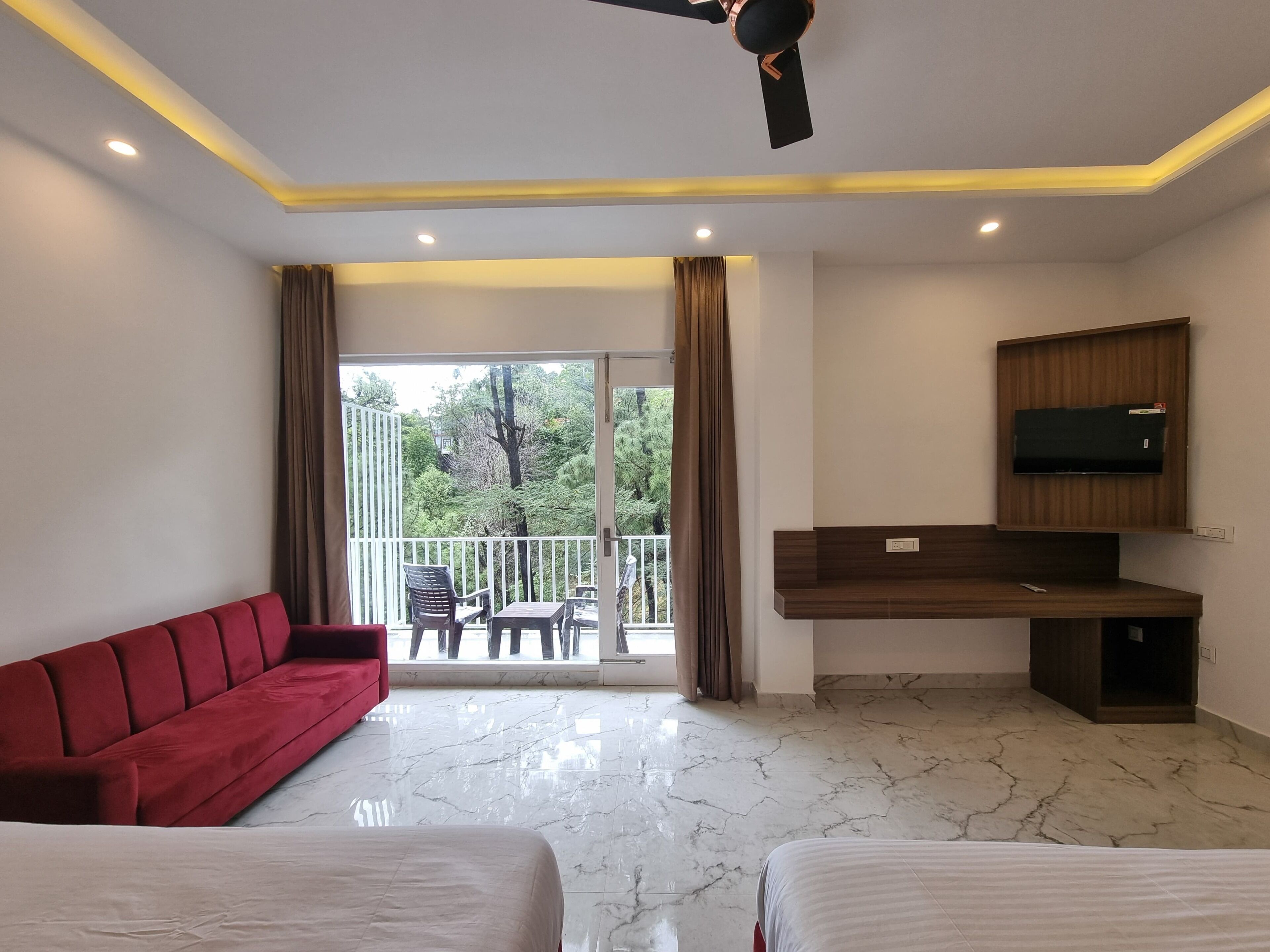 A hotel room with a balcony, a red sofa, a bed, a desk with a TV, and marble flooring.