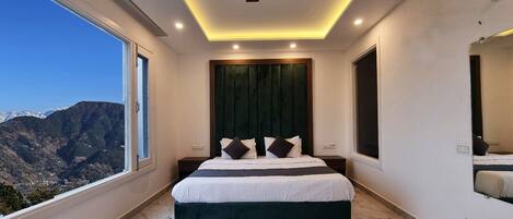 Un dormitorio con cama, ventilador de techo, ventana grande y vistas a las montañas.