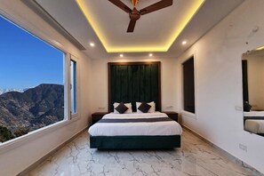 Une chambre à coucher avec un lit, un ventilateur de plafond, une grande fenêtre et une vue sur les montagnes.