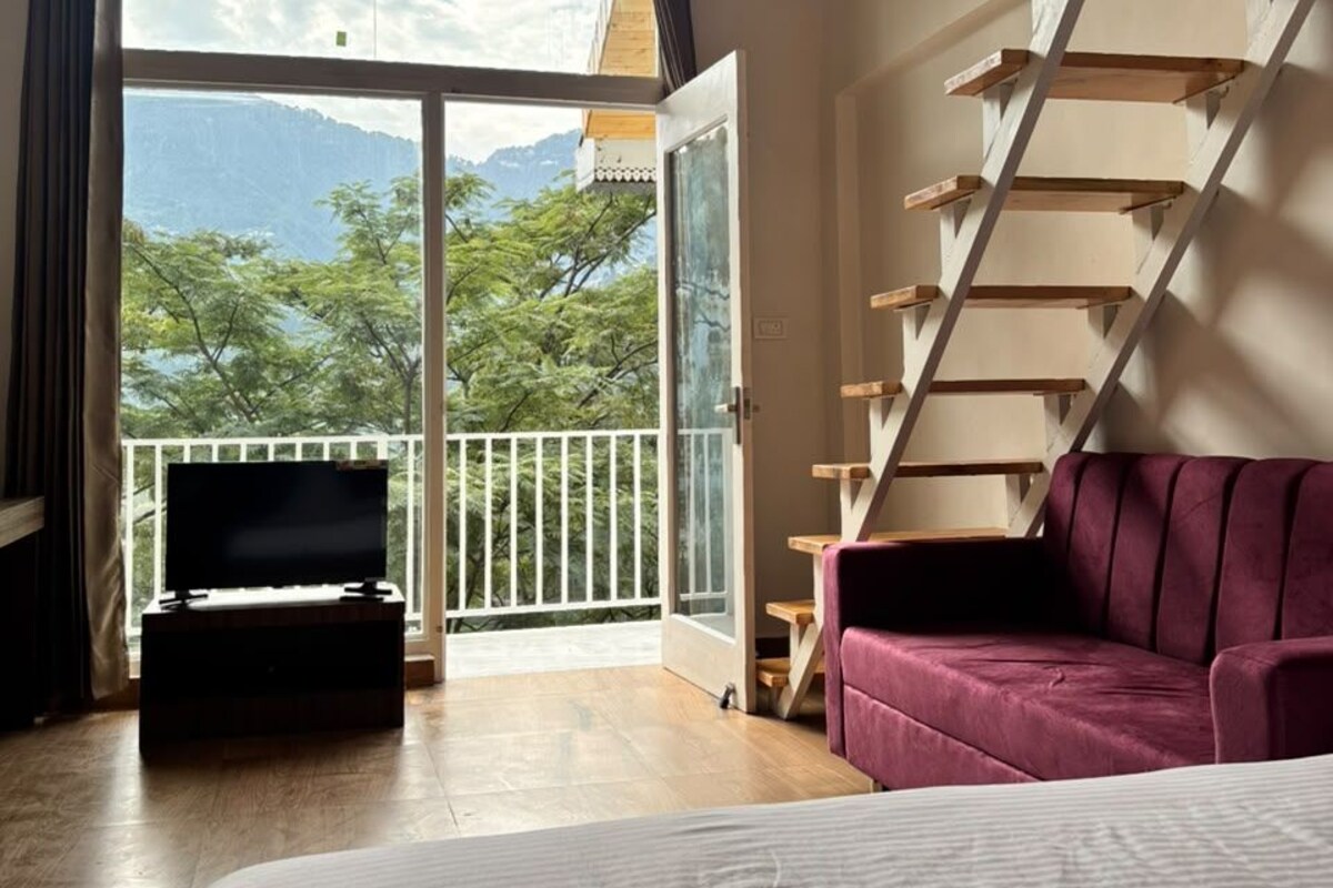 A bedroom with a large bed, a wooden staircase, and a balcony with a view of mountains.