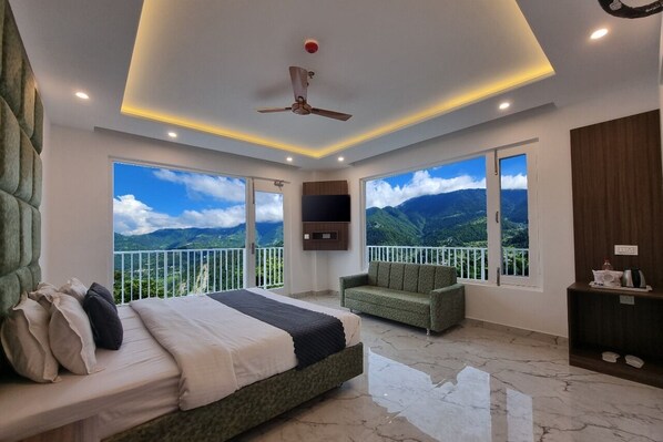 A bedroom with a bed, a sofa, a TV, and a balcony with a mountain view.