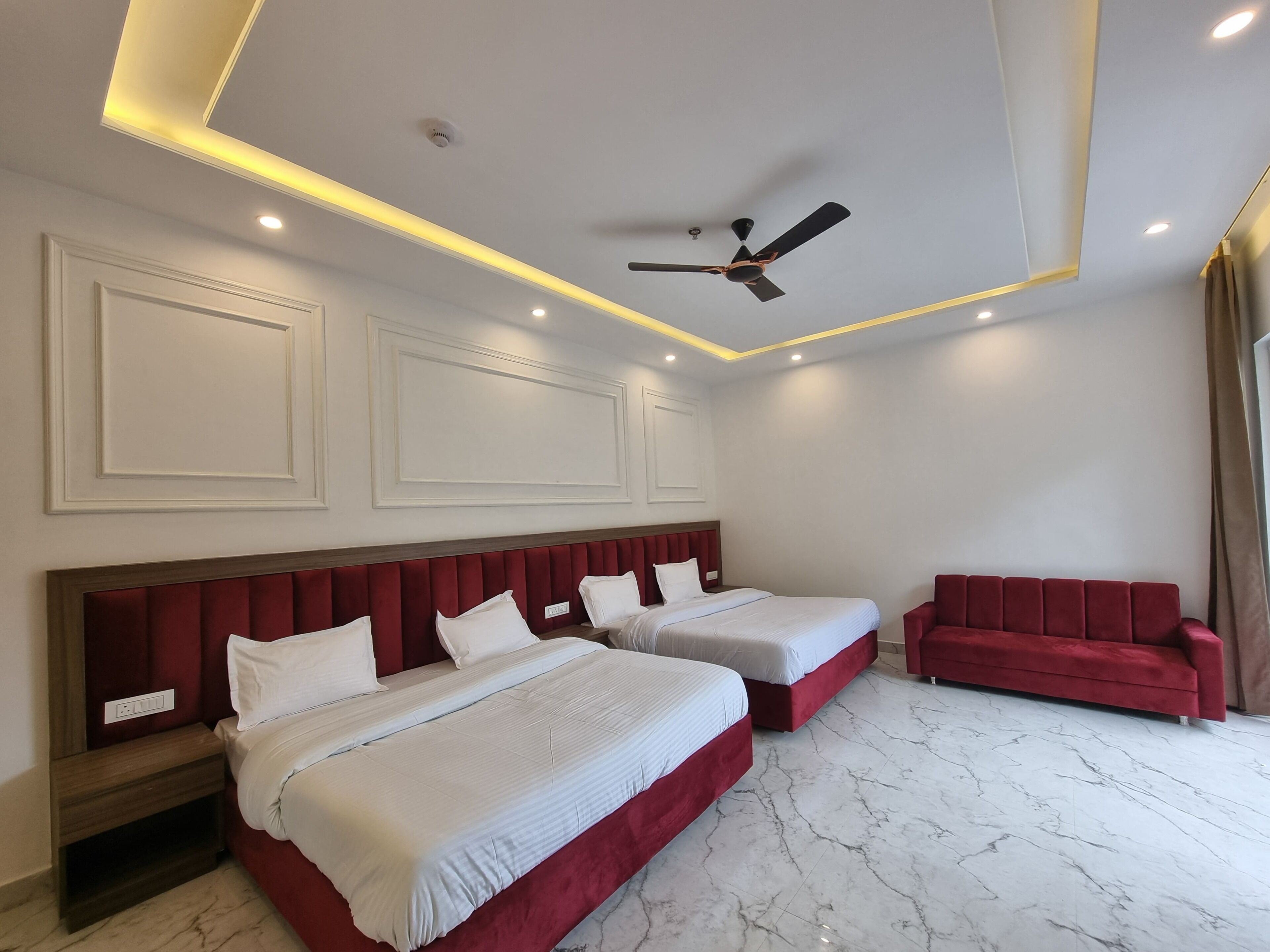 Habitación de hotel con dos camas, un sofá rojo, ventilador de techo e iluminación empotrada.