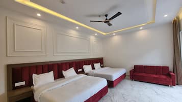 Habitación de hotel con dos camas, un sofá rojo, ventilador de techo e iluminación empotrada.