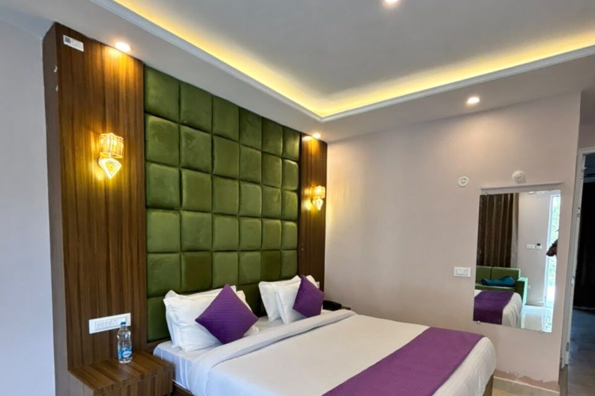 A modern hotel room with a large bed, a wooden nightstand, a green padded headboard, and a mirror on the wall.