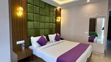 Una habitación de hotel moderna con una cama grande, una mesita de noche de madera, un cabecero acolchado verde y un espejo en la pared.