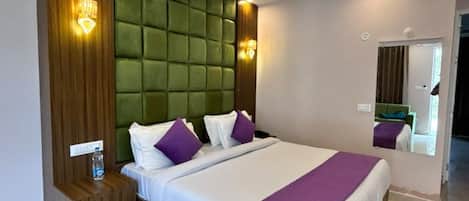 Una habitació d'hotel moderna amb un llit gran, una petita taula de nit de fusta, un reposacapses verd acolxat i un mirall a la paret.