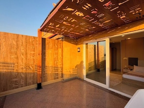Une chambre d’hôtel moderne dotée d’une grande porte-fenêtre coulissante donnant sur un balcon orné d’hiéroglyphes égyptiens.