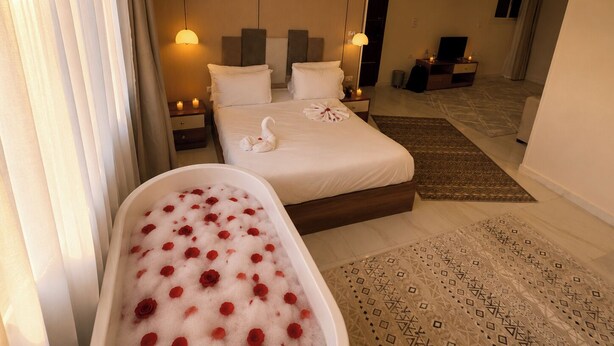 Ein Hotelzimmer mit einem großen Bett, einer Badewanne mit Rosenblättern, einem Schreibtisch und einem Fernseher.