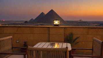 Une terrasse avec vue sur les pyramides, une table avec des chaises et une lampe.