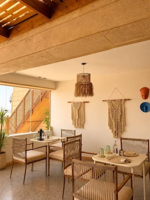 Un coin repas avec une table et des chaises, une décoration murale en macramé et un escalier.