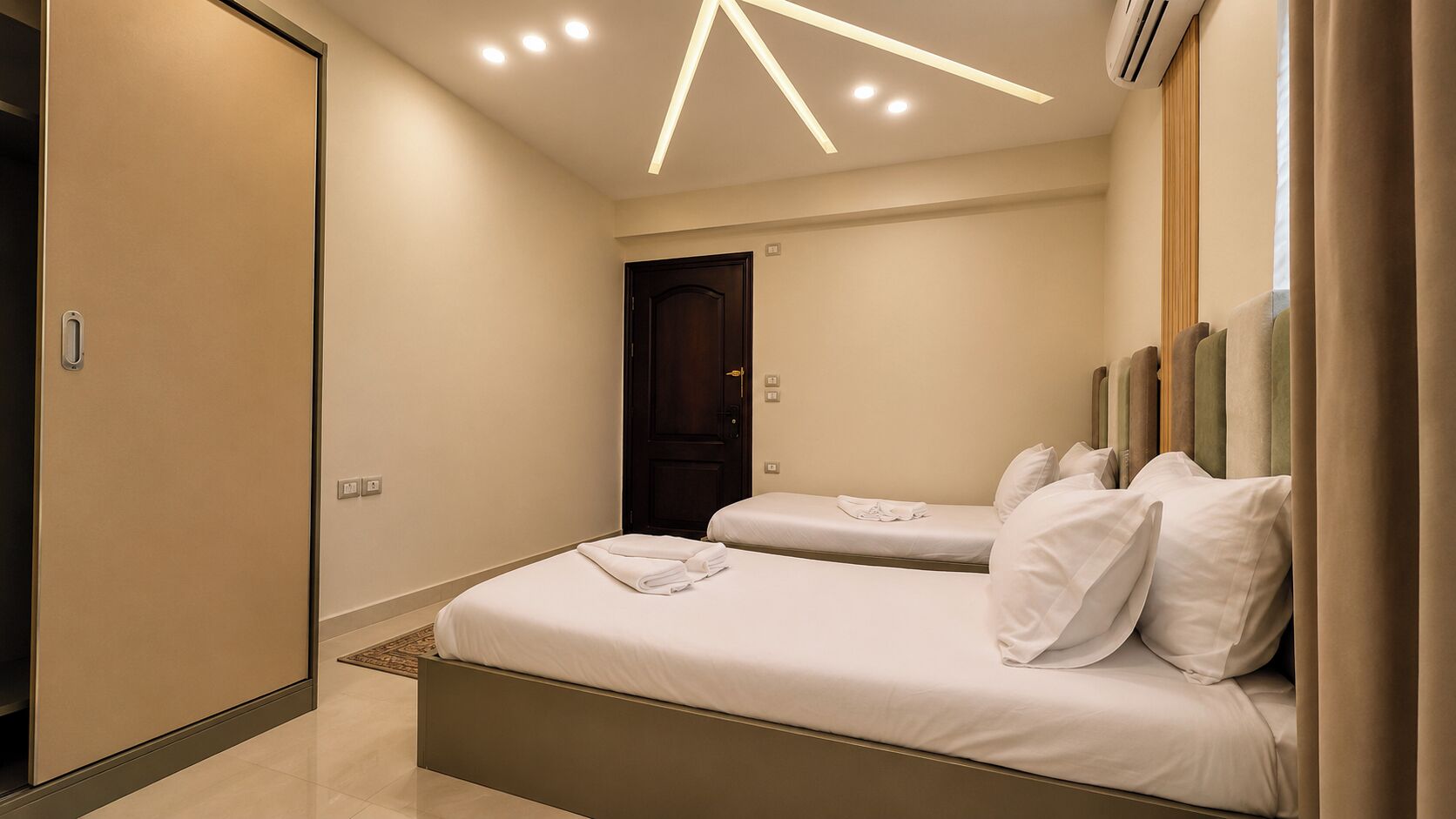 A hotel room with two beds, a wardrobe, and a door leading to another room.