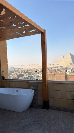 Ein Badezimmer mit einer freistehenden Badewanne, einer hölzernen Pergola und Blick auf die Pyramiden.
