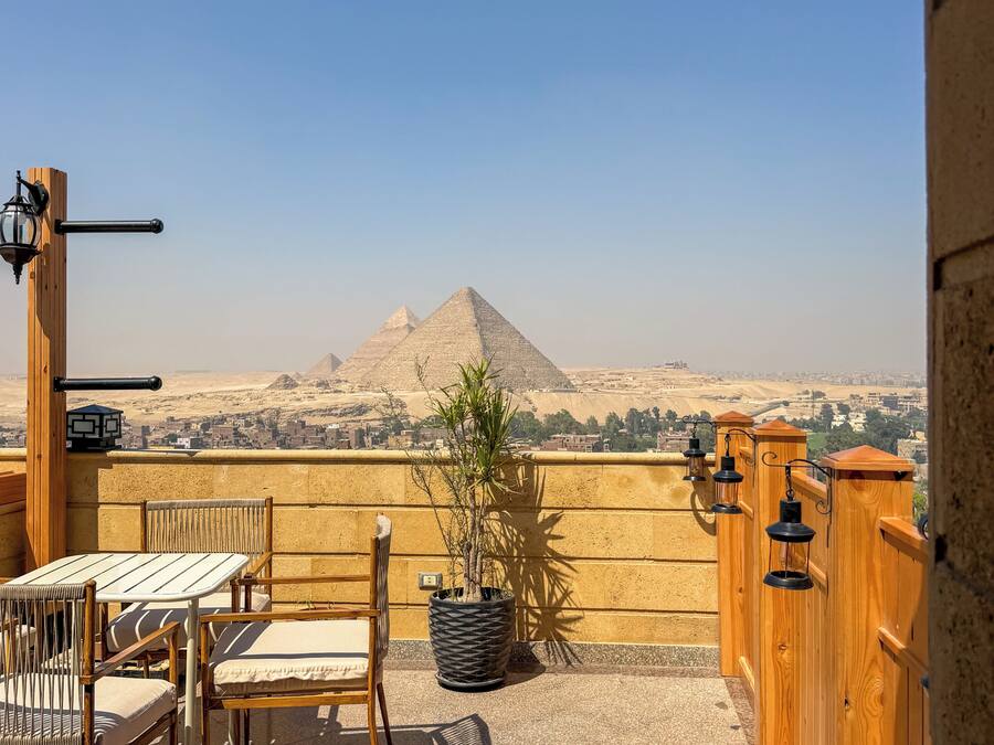 Una terraza con vistas a pirámides, muebles de madera y una planta en maceta.