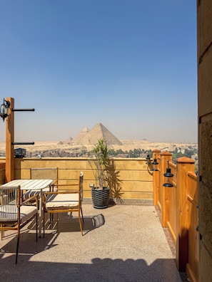 A terrace with a view of pyramids, wooden furniture, and a potted plant. - Gardenia pyramids Palace (Giza)