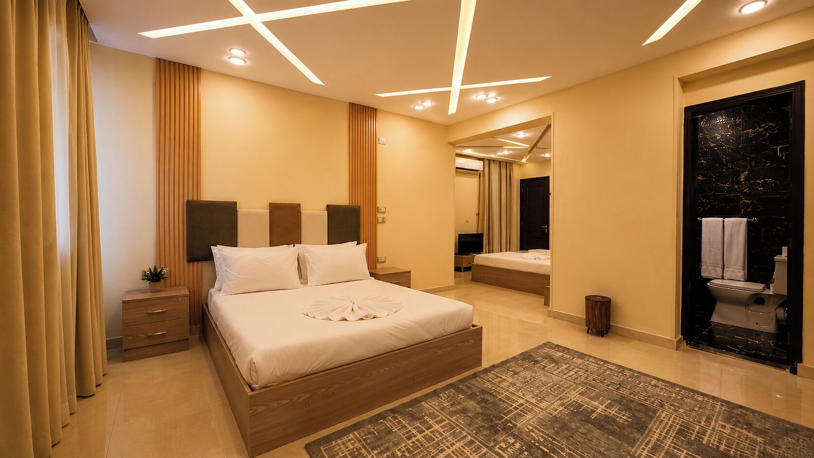 A modern bedroom with a large bed, bedside tables, a TV, and a bathroom with a toilet and sink.