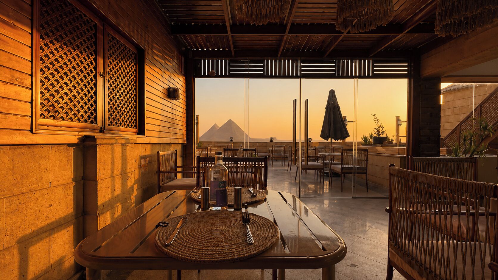 An outdoor dining area with tables and chairs, a bottle of liquor, and a view of a mountain.