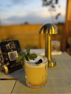 A glass of yellow beverage with mint leaves, a QR code, and a gold lamp on a table with a QR code and a menu. - Gardenia pyramids Palace (Giza)