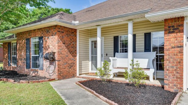 A two-story house with a brick facade, a covered porch with white chairs, and a well-maintained lawn. - 6BR Family Home Near Twin Hills Fire Pit (Crestview)