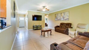 A spacious living room with a flat-screen TV, a ceiling fan, and a large painting on the wall. - 6BR Family Home Near Twin Hills Fire Pit (Crestview)