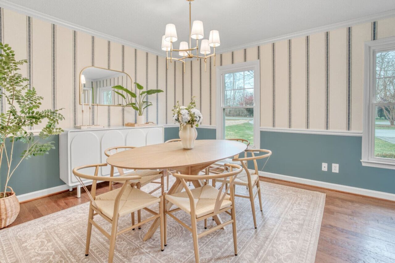 Une salle à manger avec une table ronde, six chaises, un lustre, un miroir et une vue sur l’extérieur.
