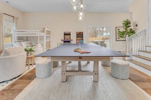 A room with a ping pong table, bunk beds, a small table with a plant, and a staircase. - Greensboro Getaway Villa (Greensboro)