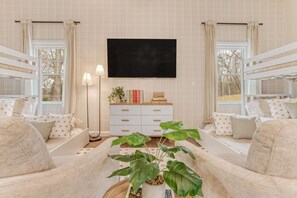A cozy room with bunk beds, a flat-screen TV, a bedside table with books, and a potted plant. - Greensboro Getaway Villa (Greensboro)