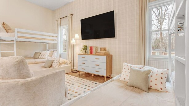 A bedroom with bunk beds, a flat-screen TV, a dresser, and a window with a view. - Greensboro Getaway Villa (Greensboro)