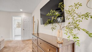 A room with a wooden dresser, a large mirror, and a wall-mounted TV. - Greensboro Getaway Villa (Greensboro)