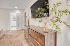 A room with a wooden dresser, a large mirror, and a wall-mounted TV. - Greensboro Getaway Villa (Greensboro)