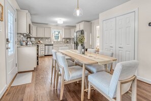 A modern kitchen with white cabinets, a wooden dining table, and striped chairs. - Greensboro Getaway Villa (Greensboro)
