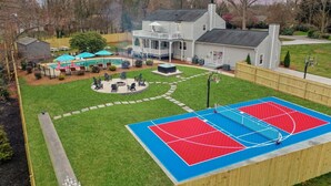 A residential property with a basketball court, a covered patio, and a large house with a porch. - Greensboro Getaway Villa (Greensboro)
