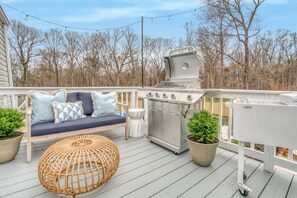 An outdoor deck with a grill, seating area, and potted plants. - Greensboro Getaway Villa (Greensboro)