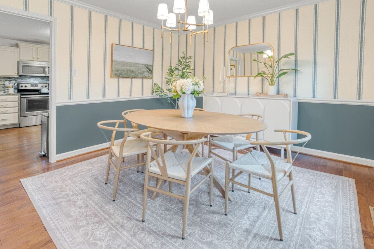 Ein Essbereich mit einem runden Tisch, sechs Stühlen, einer Blumenvase, einer Chandelüster und einer Küche im Hintergrund.